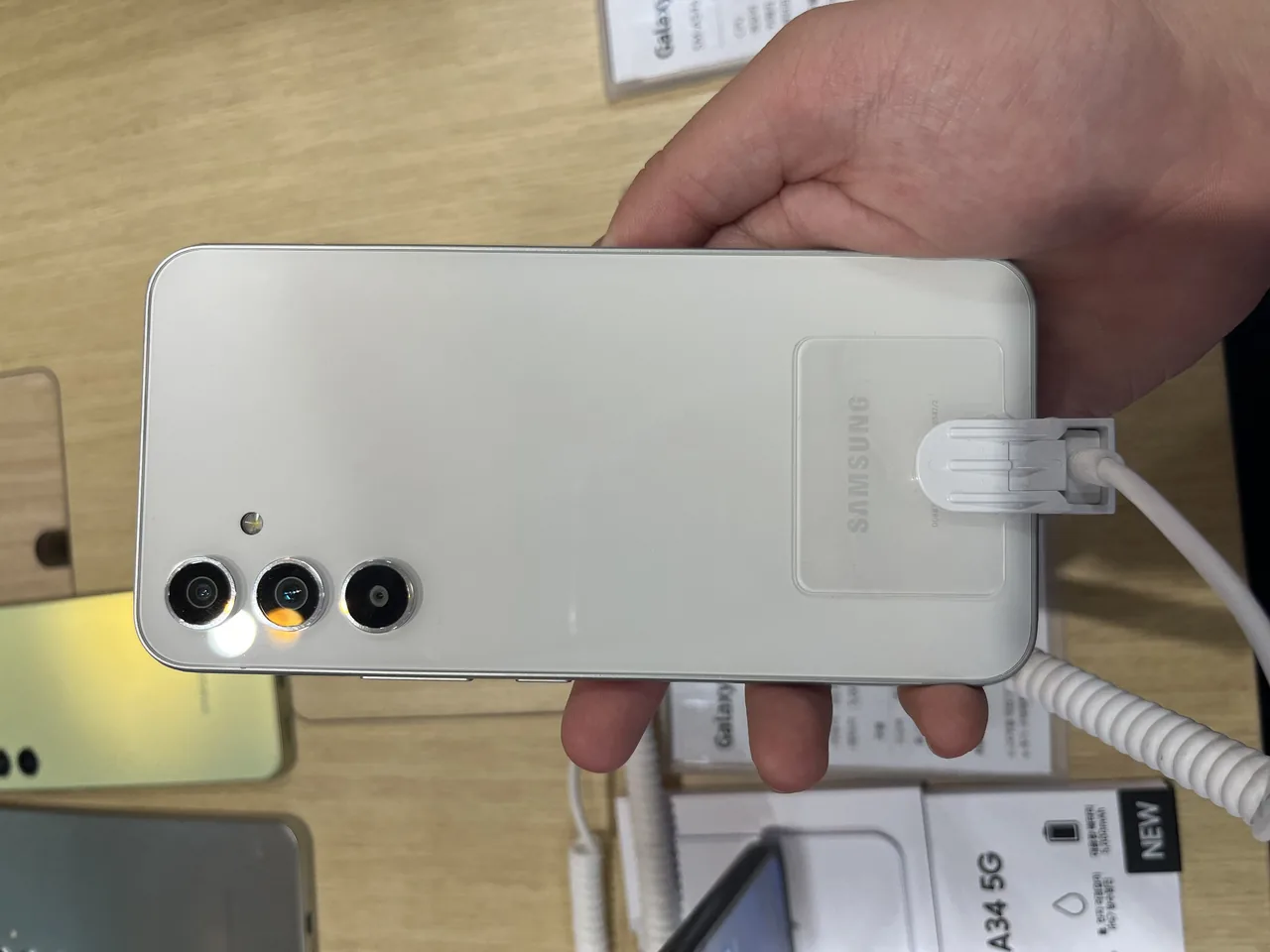 Dos blanc d’un Samsung Galaxy A54 tenu dans une main au-dessus d’une table