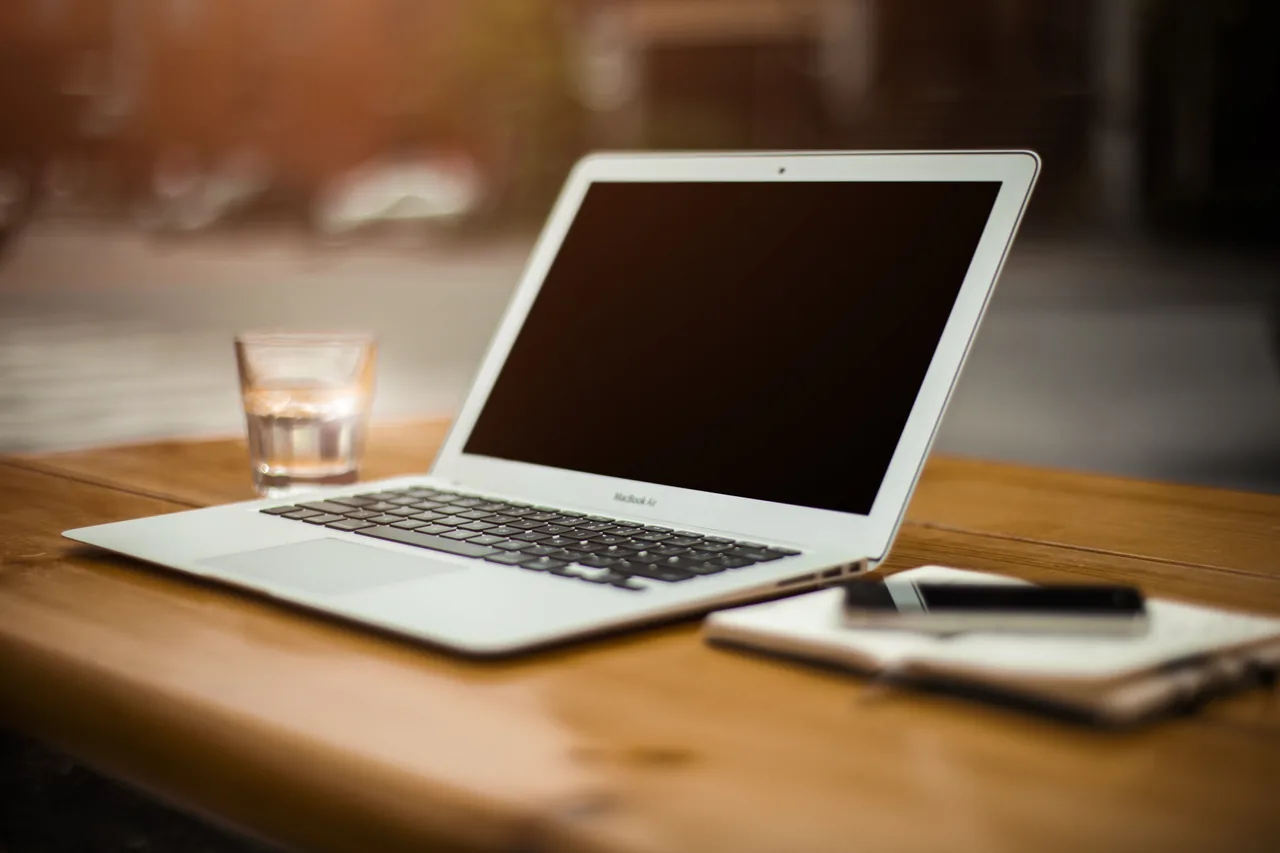 Ordinateur portable en aluminium sur une table en bois, avec un verre et un carnet
